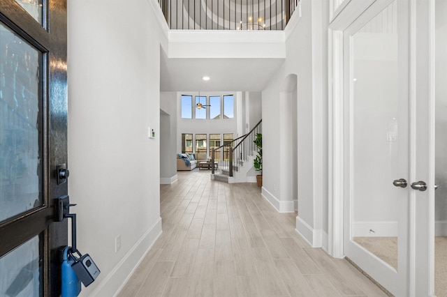 entrance foyer featuring stairs, a high ceiling, light wood-type flooring, and baseboards