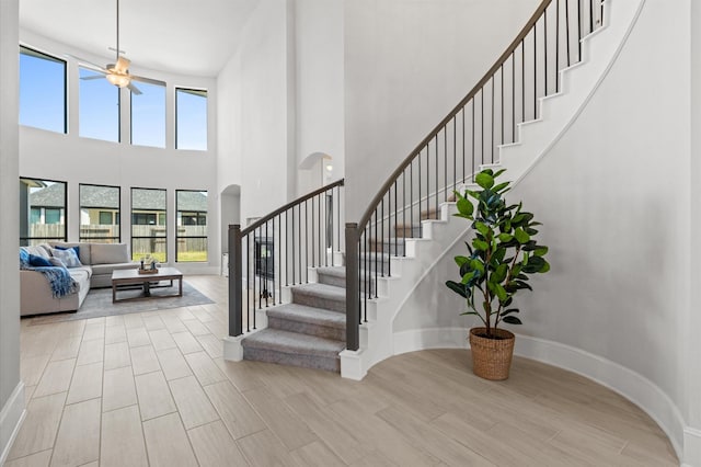 stairs featuring a ceiling fan, wood tiled floor, arched walkways, and baseboards