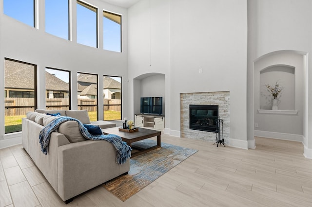 living room featuring baseboards, a stone fireplace, light wood-style flooring, and a healthy amount of sunlight