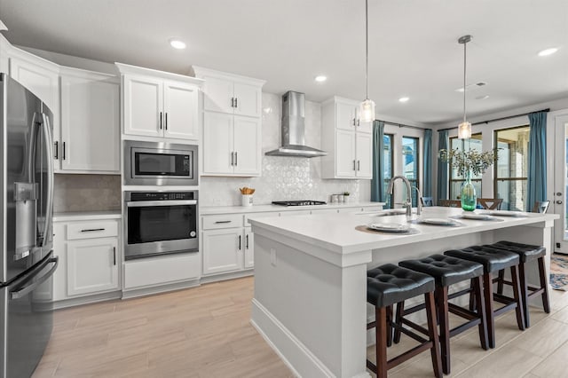 kitchen featuring wall chimney exhaust hood, light countertops, white cabinets, and stainless steel appliances