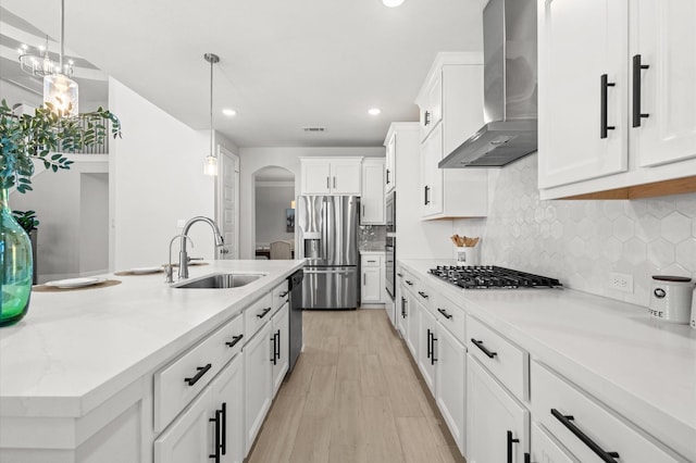 kitchen with arched walkways, stainless steel appliances, a sink, white cabinets, and wall chimney range hood