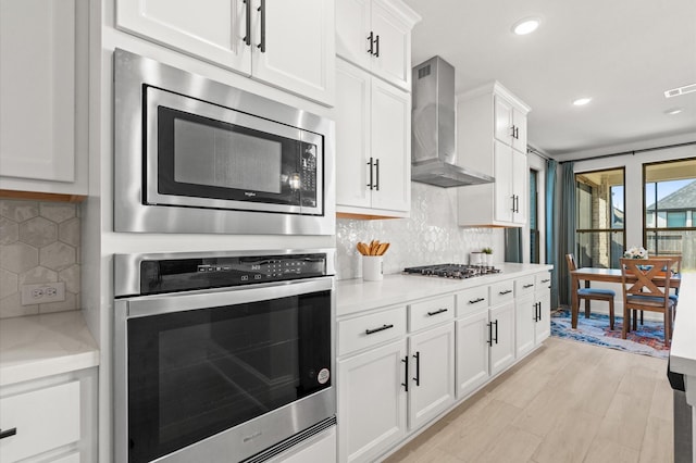 kitchen featuring stainless steel appliances, white cabinets, wall chimney range hood, and tasteful backsplash