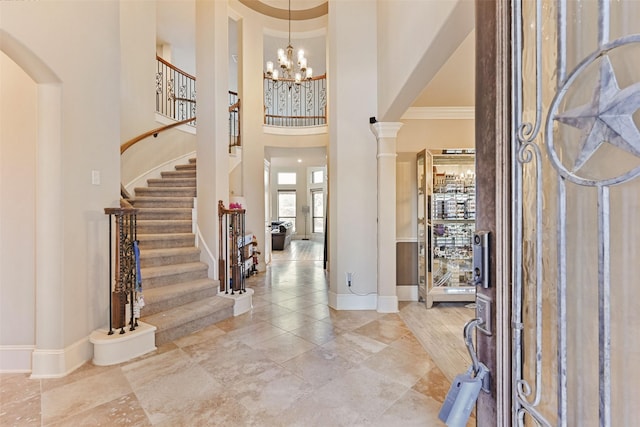 foyer entrance featuring baseboards, a towering ceiling, stairway, ornamental molding, and an inviting chandelier