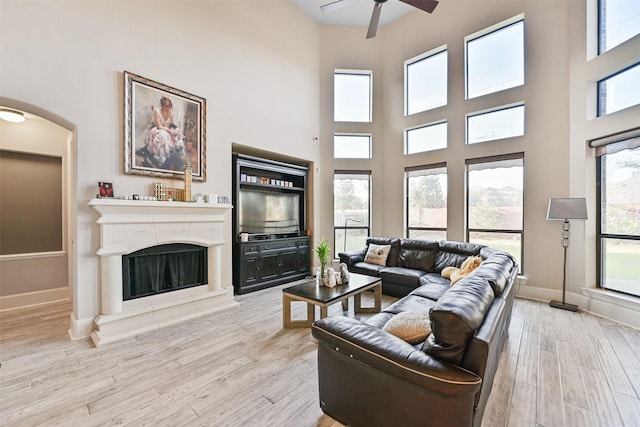 living area featuring baseboards, a fireplace with raised hearth, a ceiling fan, wood finished floors, and a high ceiling