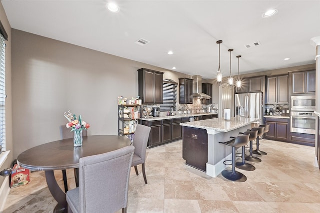 kitchen with stainless steel appliances, visible vents, backsplash, dark brown cabinetry, and wall chimney range hood