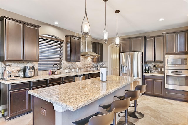 kitchen featuring dark brown cabinetry, a sink, appliances with stainless steel finishes, a center island, and wall chimney exhaust hood