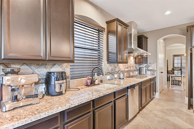 kitchen featuring arched walkways, stainless steel appliances, tasteful backsplash, a sink, and wall chimney exhaust hood