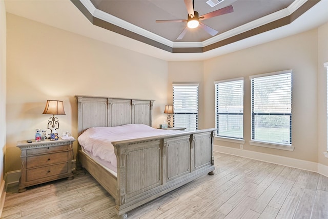 bedroom featuring ornamental molding, a tray ceiling, light wood-style flooring, and baseboards