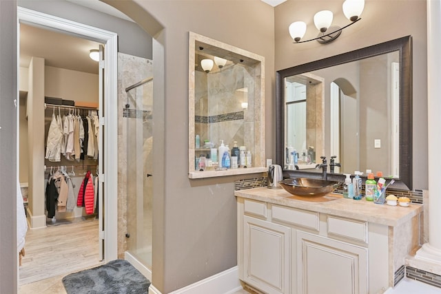 bathroom with a stall shower, a walk in closet, vanity, and baseboards