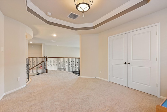 carpeted empty room featuring a tray ceiling, visible vents, crown molding, and baseboards