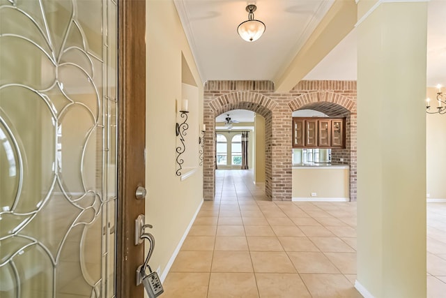 foyer with brick wall, arched walkways, baseboards, and light tile patterned flooring