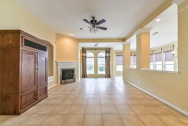 unfurnished living room featuring light tile patterned floors, baseboards, ceiling fan, ornate columns, and a fireplace