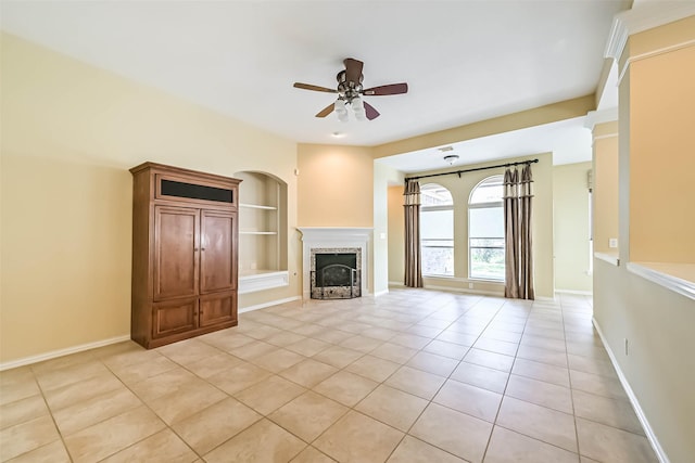 unfurnished living room featuring baseboards, ceiling fan, built in shelves, a fireplace, and light tile patterned flooring