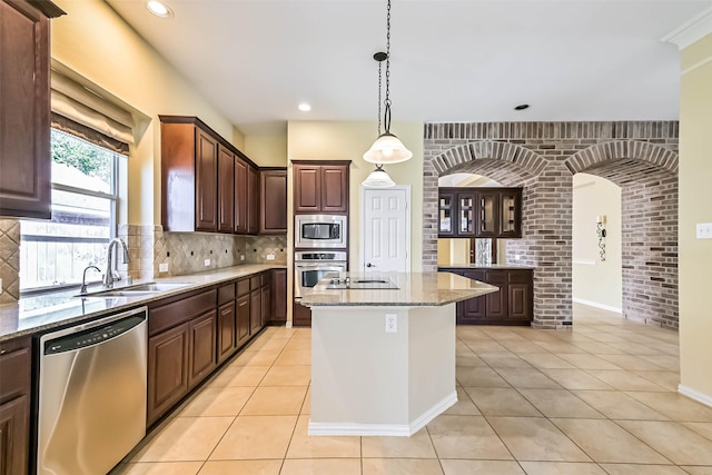 kitchen featuring light tile patterned flooring, light stone countertops, a sink, appliances with stainless steel finishes, and decorative backsplash