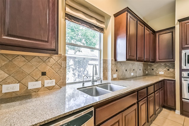 kitchen featuring light tile patterned floors, stainless steel appliances, a sink, light stone countertops, and tasteful backsplash