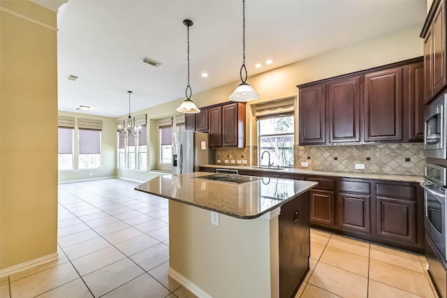 kitchen featuring light tile patterned floors, stainless steel appliances, decorative backsplash, a sink, and a kitchen island