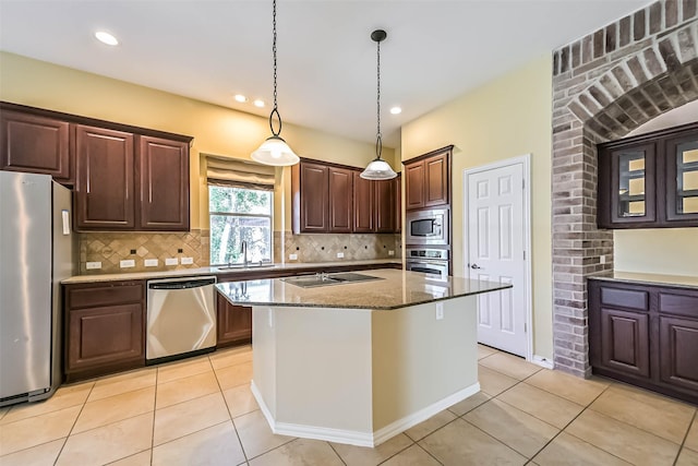 kitchen featuring stone counters, decorative light fixtures, tasteful backsplash, appliances with stainless steel finishes, and a sink