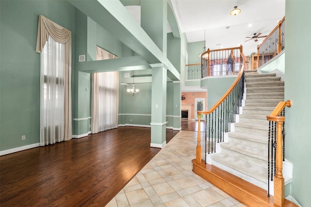 interior space with ceiling fan with notable chandelier, a fireplace, a high ceiling, and wood finished floors