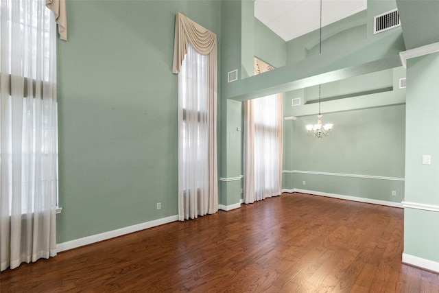 unfurnished room featuring a notable chandelier, visible vents, wood finished floors, high vaulted ceiling, and plenty of natural light