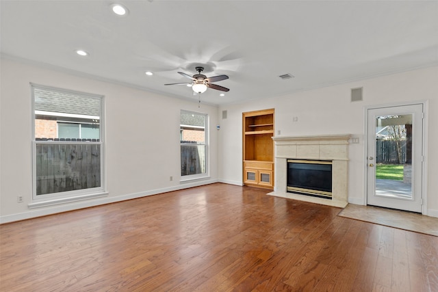 unfurnished living room featuring built in shelves, a tile fireplace, baseboards, and hardwood / wood-style floors