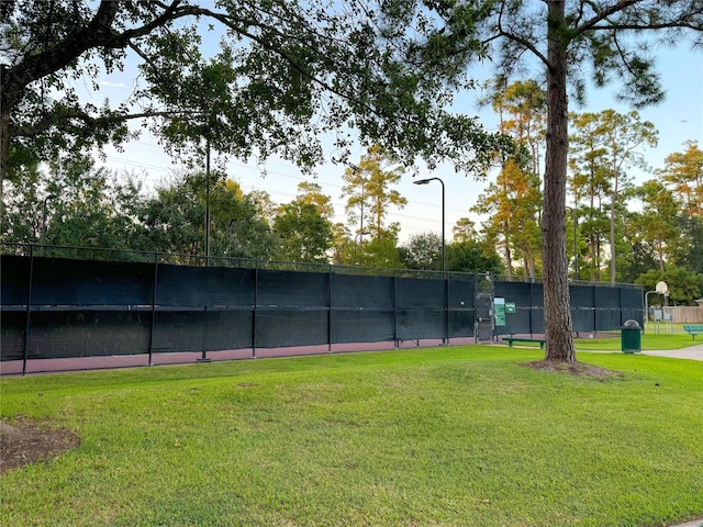 view of tennis court with fence and a lawn