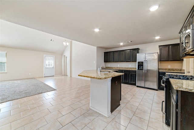 kitchen with an island with sink, light stone counters, appliances with stainless steel finishes, open floor plan, and a sink