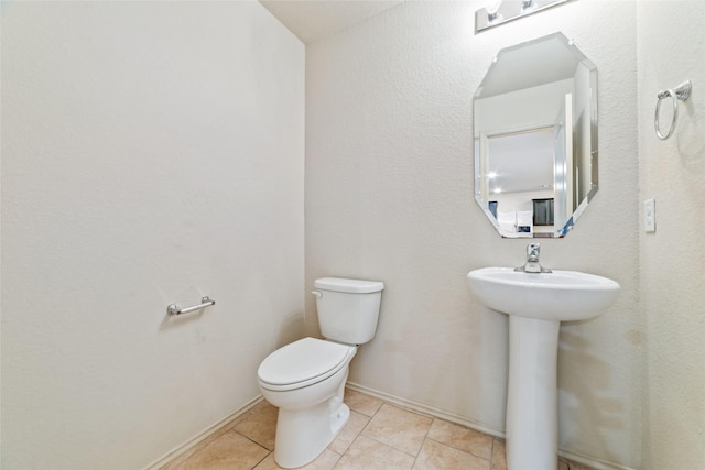 half bathroom featuring toilet, baseboards, a sink, and tile patterned floors