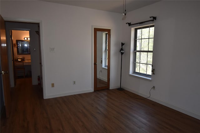 unfurnished bedroom featuring ensuite bath, dark wood finished floors, and baseboards