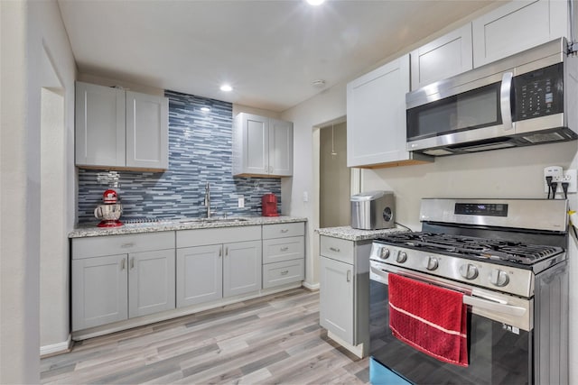 kitchen featuring stainless steel appliances, a sink, backsplash, light stone countertops, and light wood finished floors