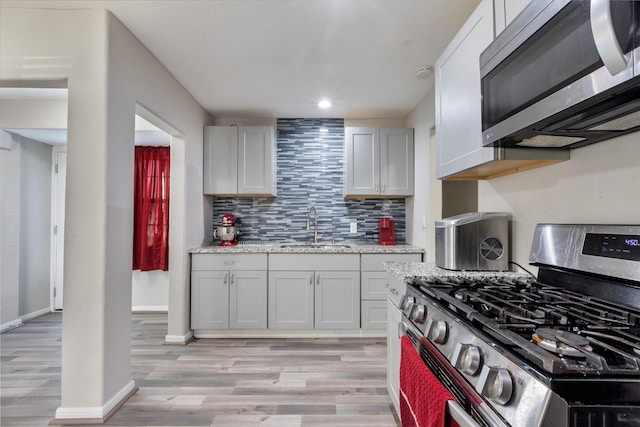 kitchen featuring backsplash, appliances with stainless steel finishes, a sink, light wood-type flooring, and baseboards