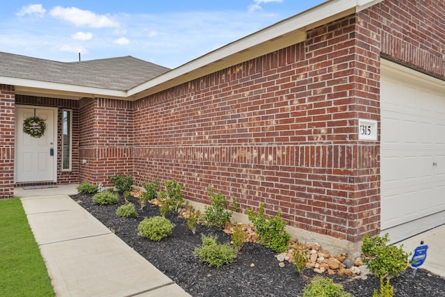 property entrance with brick siding, roof with shingles, and an attached garage