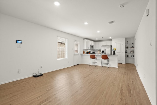 kitchen featuring stainless steel appliances, white cabinetry, light wood-type flooring, a peninsula, and a kitchen bar