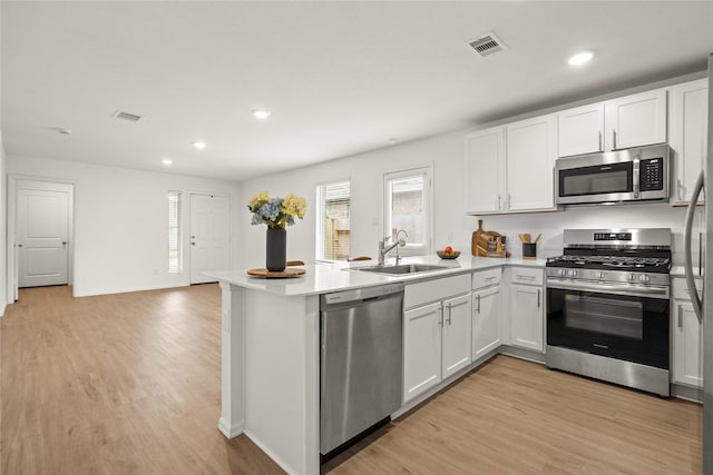 kitchen with stainless steel appliances, a peninsula, a sink, visible vents, and light wood-style floors