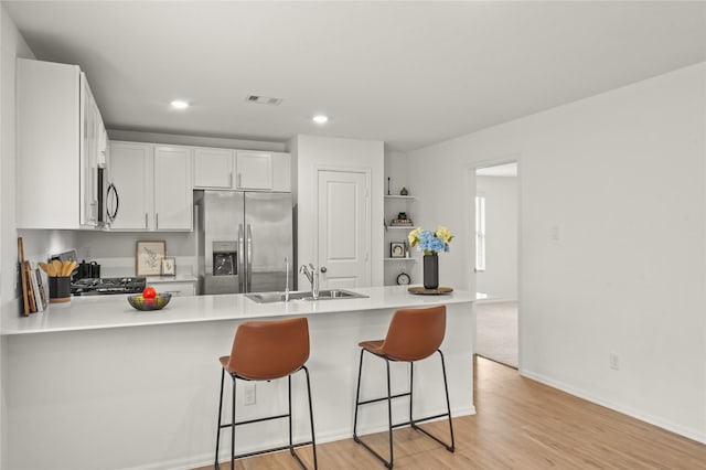 kitchen featuring a breakfast bar, stainless steel appliances, white cabinetry, a sink, and a peninsula