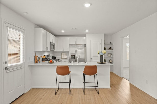 kitchen with open shelves, light countertops, appliances with stainless steel finishes, light wood-style floors, and a peninsula