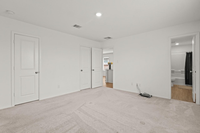 unfurnished bedroom featuring ensuite bath, carpet flooring, and visible vents