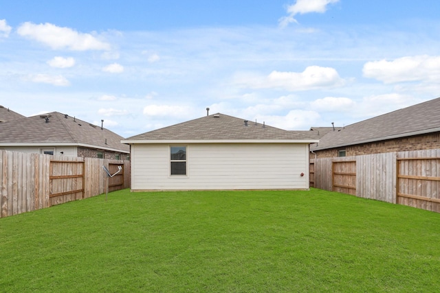 rear view of house with a fenced backyard, a shingled roof, and a lawn