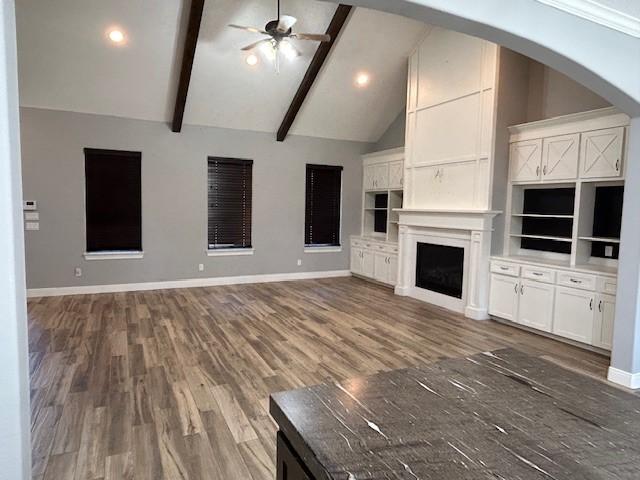 unfurnished living room featuring high vaulted ceiling, beam ceiling, baseboards, and a ceiling fan