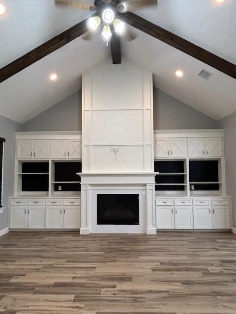 unfurnished living room featuring light wood-type flooring, vaulted ceiling with beams, ceiling fan, and a fireplace