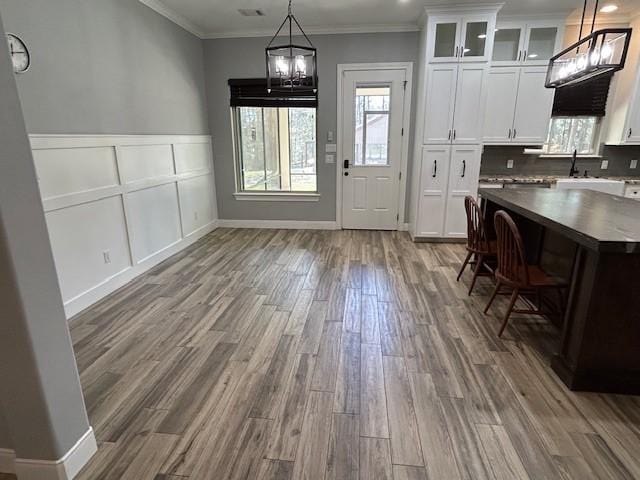 unfurnished dining area with ornamental molding, wood finished floors, a chandelier, a decorative wall, and a sink