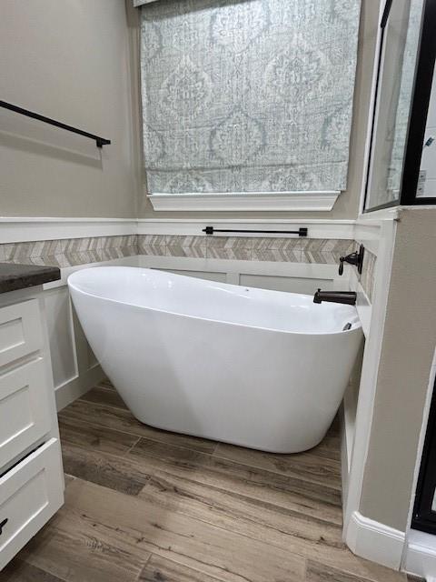 bathroom with a wainscoted wall, wood finished floors, and a soaking tub