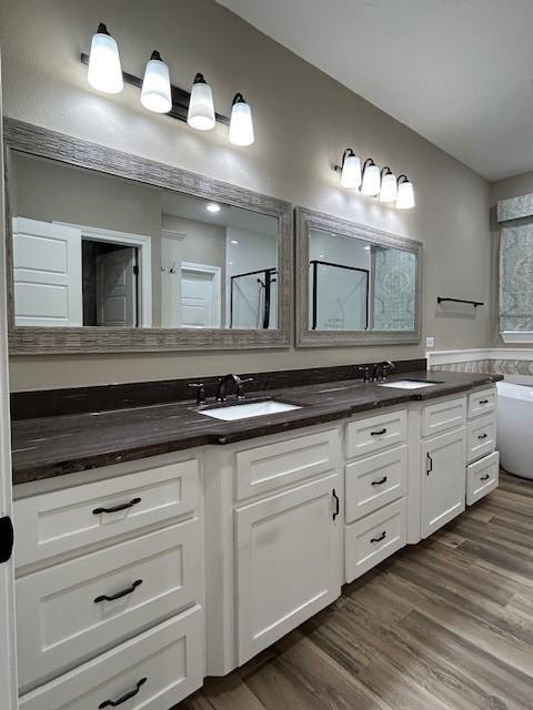 bathroom featuring double vanity, wood finished floors, a sink, and a bathing tub