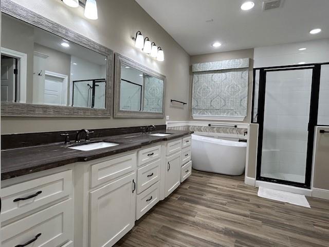 bathroom featuring wood finished floors, a sink, visible vents, a freestanding bath, and a shower stall