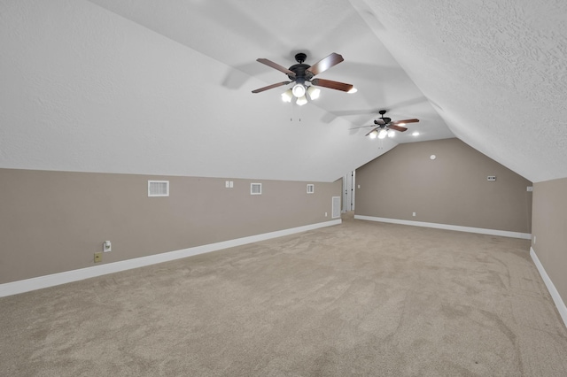 bonus room featuring a textured ceiling, lofted ceiling, light carpet, visible vents, and baseboards