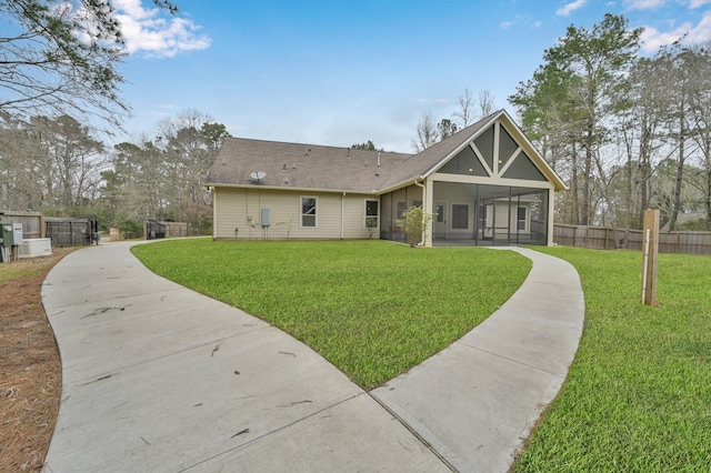 rear view of house featuring a sunroom, fence, a lawn, and roof with shingles