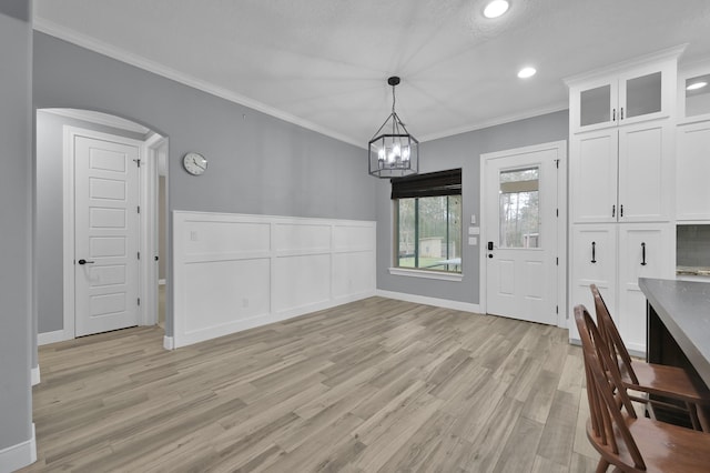 unfurnished dining area featuring arched walkways, recessed lighting, crown molding, light wood finished floors, and an inviting chandelier