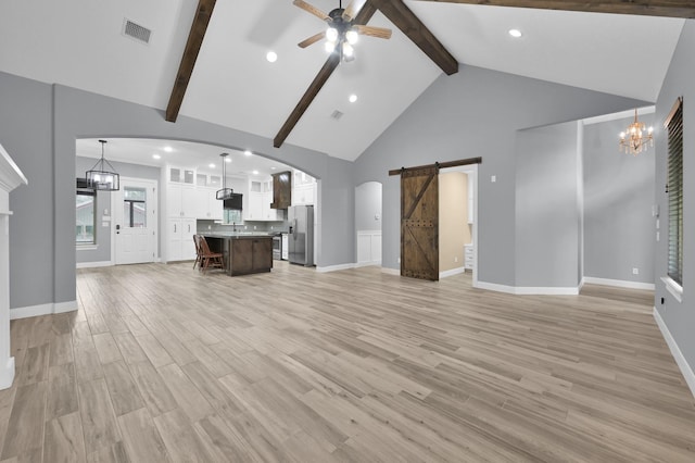 unfurnished living room with a barn door, ceiling fan with notable chandelier, visible vents, light wood-style floors, and beamed ceiling