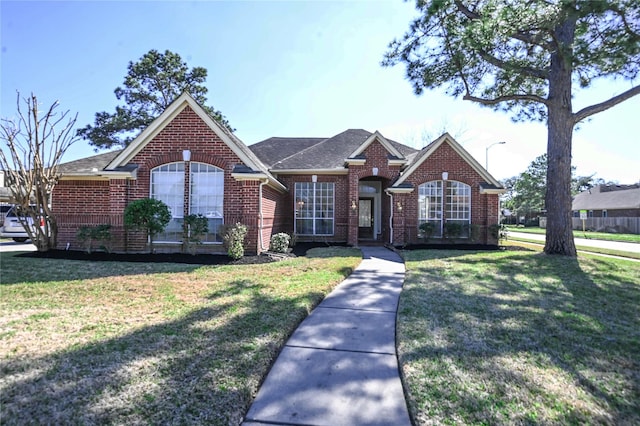 view of front facade with brick siding, a front lawn, and roof with shingles