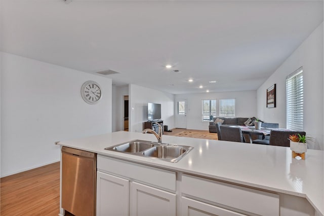 kitchen featuring visible vents, open floor plan, stainless steel dishwasher, white cabinetry, and a sink