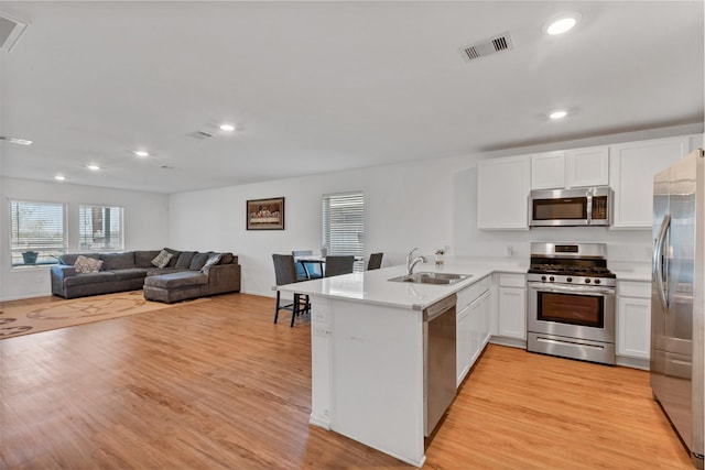 kitchen with visible vents, light wood-style flooring, appliances with stainless steel finishes, a sink, and a peninsula